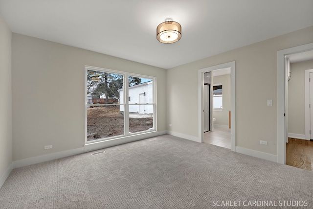 unfurnished bedroom featuring carpet floors, multiple windows, visible vents, and baseboards