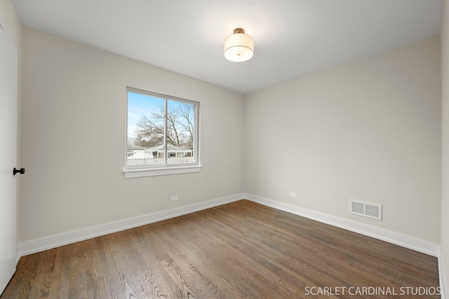 empty room with dark wood-style flooring, visible vents, and baseboards