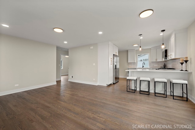 kitchen featuring tasteful backsplash, open floor plan, dark wood-type flooring, a peninsula, and stainless steel refrigerator with ice dispenser