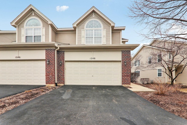 view of property featuring aphalt driveway, brick siding, and a garage