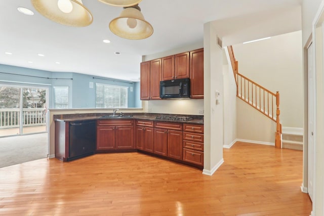 kitchen featuring dark countertops, black appliances, light wood-style floors, and a sink