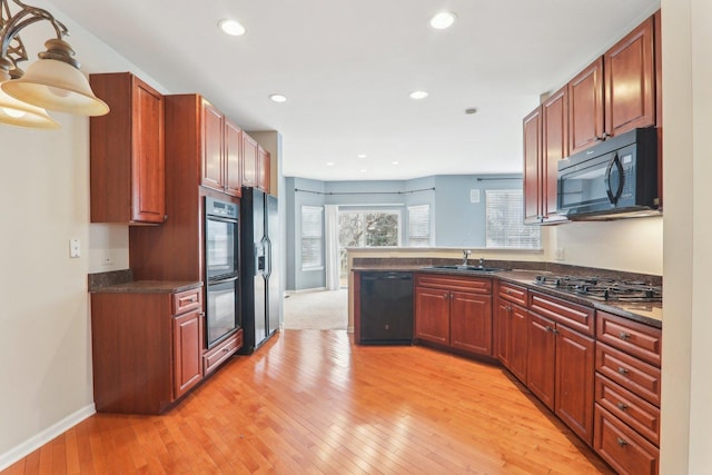 kitchen with light wood-style flooring, a peninsula, black appliances, a sink, and recessed lighting