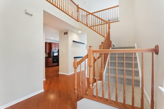 stairs featuring a high ceiling, wood-type flooring, visible vents, and baseboards