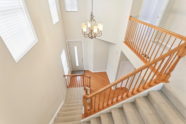 stairway with a healthy amount of sunlight, a high ceiling, baseboards, and a chandelier