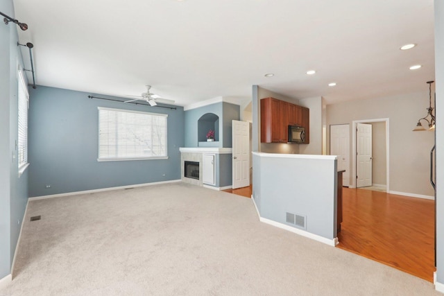 unfurnished living room with ceiling fan, light colored carpet, visible vents, baseboards, and a tiled fireplace