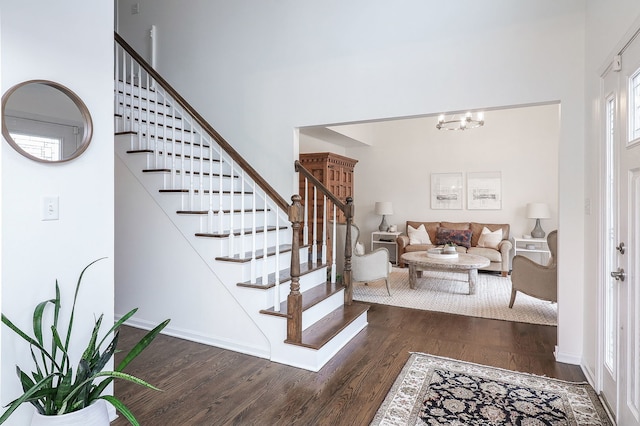 foyer entrance featuring dark wood finished floors, stairway, a towering ceiling, an inviting chandelier, and baseboards