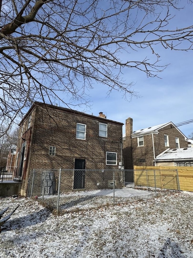 snow covered property with a fenced front yard, a chimney, and brick siding