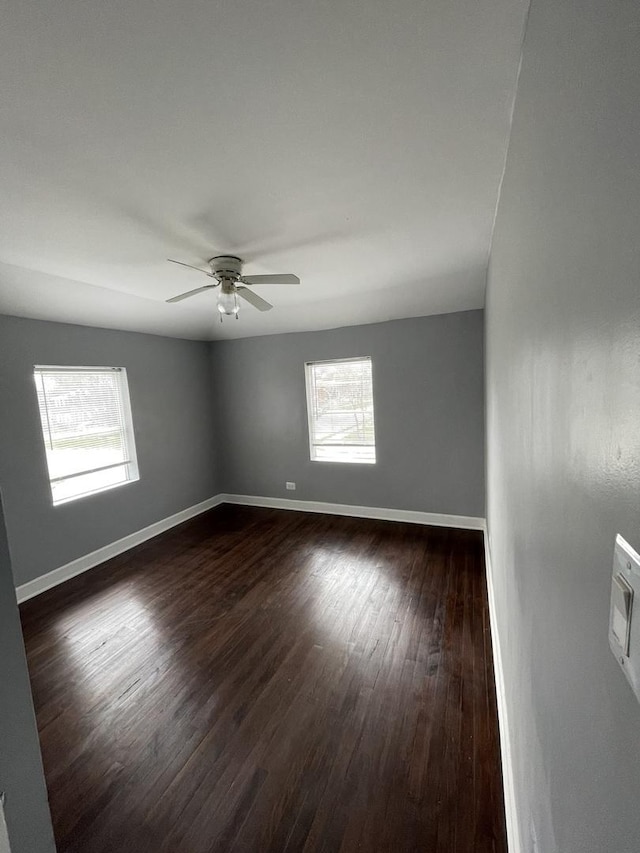 empty room featuring a ceiling fan, plenty of natural light, baseboards, and dark wood-style flooring