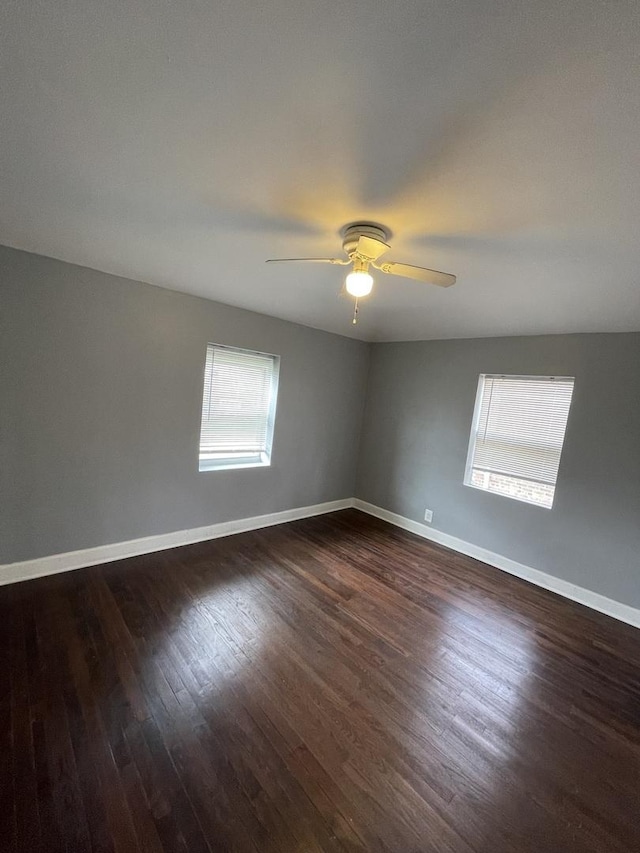 spare room featuring dark wood-style flooring, a ceiling fan, and baseboards