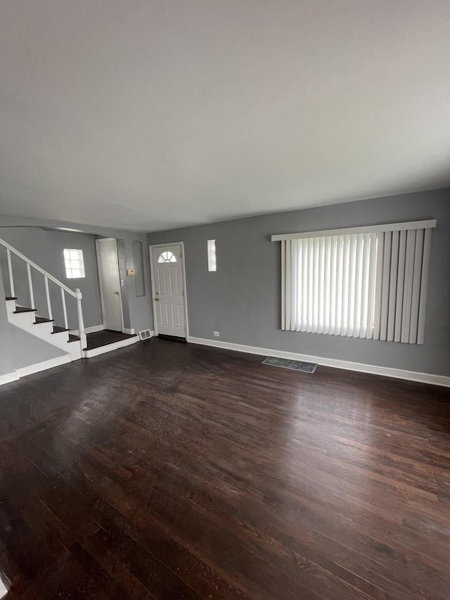 unfurnished living room with baseboards, visible vents, stairway, and wood finished floors