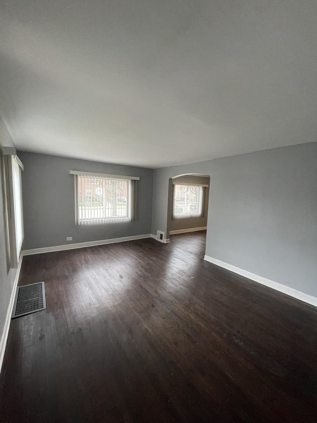 unfurnished room featuring baseboards, visible vents, and dark wood finished floors