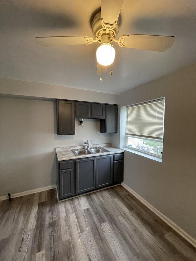 kitchen with baseboards, ceiling fan, wood finished floors, light countertops, and a sink