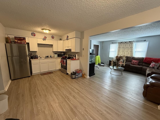 kitchen featuring a textured ceiling, stainless steel appliances, white cabinetry, open floor plan, and light wood finished floors