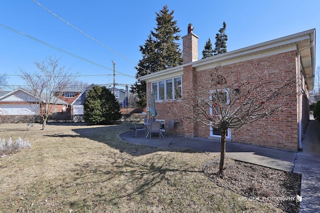 exterior space featuring a yard, a patio, brick siding, and a chimney