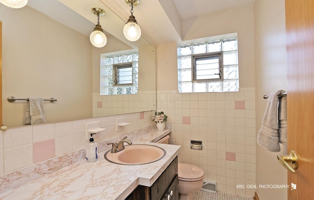 bathroom featuring vanity, a wainscoted wall, visible vents, tile walls, and toilet