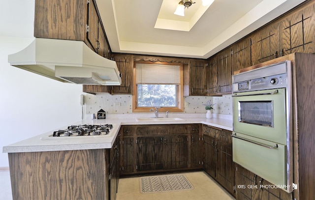 kitchen featuring premium range hood, light countertops, a tray ceiling, white appliances, and a sink