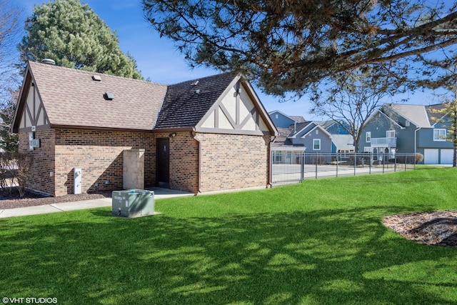 exterior space featuring roof with shingles, brick siding, a lawn, and fence