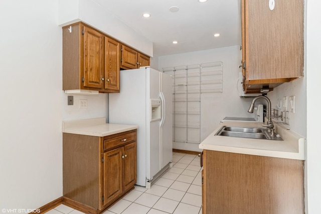 kitchen featuring recessed lighting, light countertops, brown cabinetry, a sink, and white fridge with ice dispenser