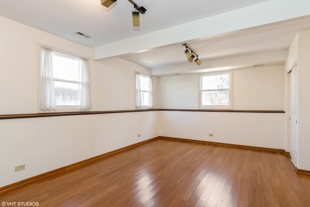 spare room featuring plenty of natural light, wood-type flooring, visible vents, and baseboards