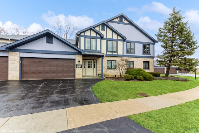 tudor home with a garage, a front lawn, brick siding, and aphalt driveway