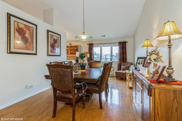 dining area featuring light wood-style floors, baseboards, visible vents, and vaulted ceiling