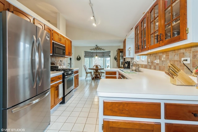 kitchen featuring light tile patterned floors, a peninsula, a sink, vaulted ceiling, and appliances with stainless steel finishes