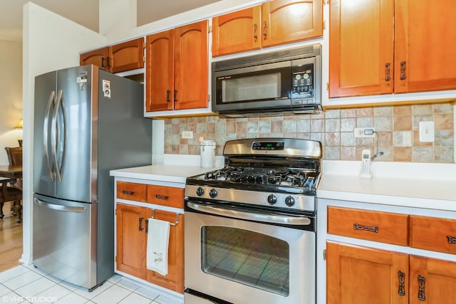 kitchen with brown cabinetry, stainless steel appliances, light countertops, backsplash, and light tile patterned flooring