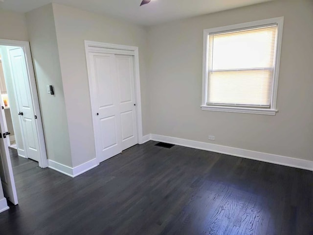 unfurnished bedroom featuring dark wood-style flooring, a closet, visible vents, and baseboards