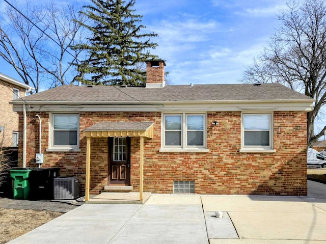 view of front facade featuring roof with shingles, brick siding, a chimney, a patio, and central AC