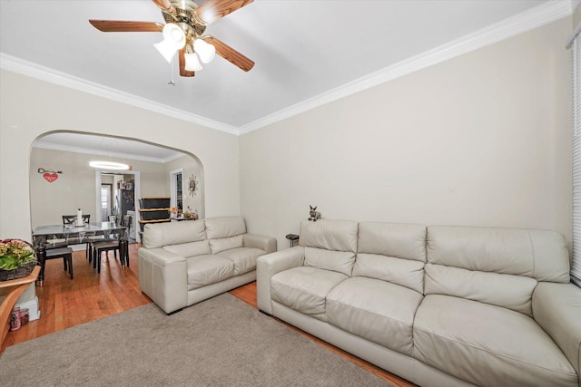 living area featuring crown molding, arched walkways, ceiling fan, and wood finished floors