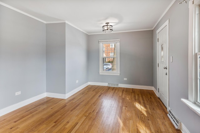 empty room featuring crown molding, light wood-type flooring, visible vents, and baseboards