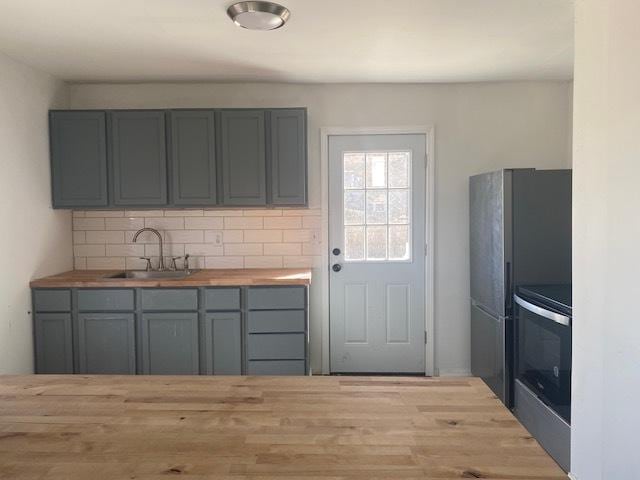 kitchen featuring butcher block counters, stainless steel appliances, a sink, and gray cabinetry