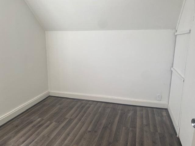 additional living space featuring dark wood-type flooring, lofted ceiling, and baseboards