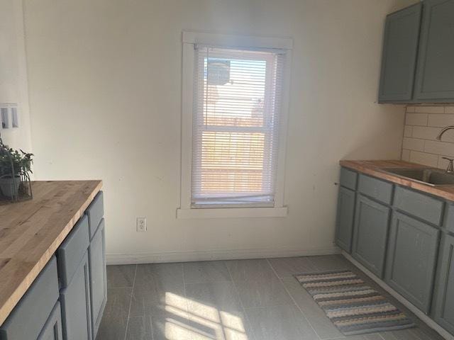 kitchen featuring baseboards, backsplash, a sink, and gray cabinetry