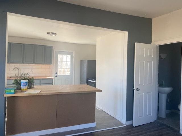 kitchen with a peninsula, gray cabinets, freestanding refrigerator, decorative backsplash, and dark wood finished floors