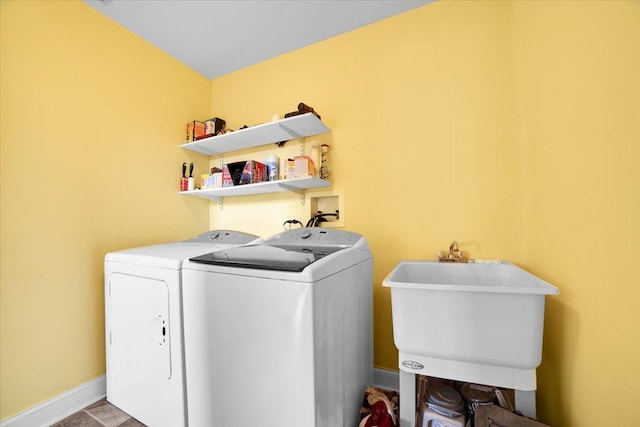 washroom with laundry area, baseboards, washer and clothes dryer, and a sink