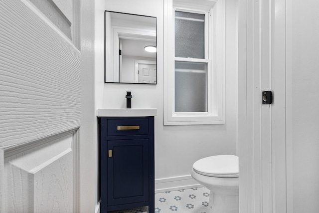 half bath with baseboards, vanity, and toilet