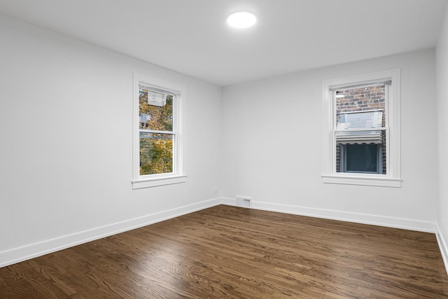 unfurnished room with a healthy amount of sunlight, visible vents, baseboards, and dark wood-type flooring