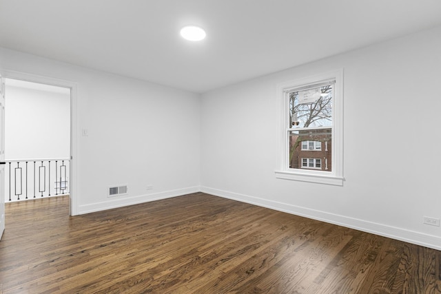 empty room featuring dark wood finished floors, visible vents, and baseboards