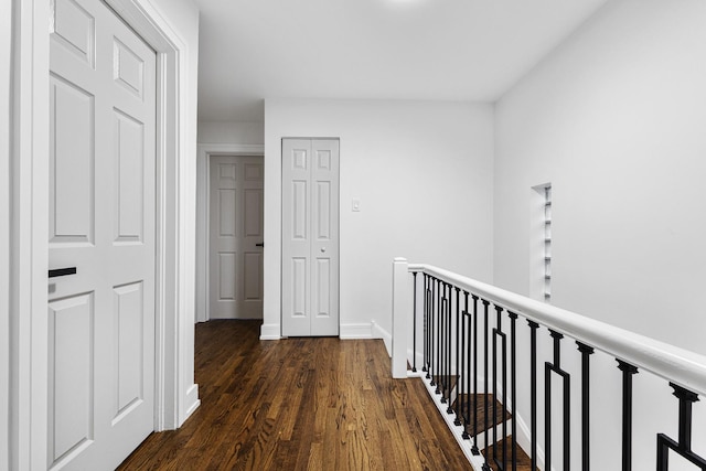 corridor with dark wood-type flooring, an upstairs landing, and baseboards