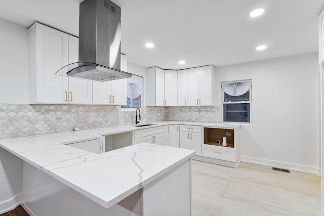 kitchen with light stone counters, island exhaust hood, white cabinets, a sink, and a peninsula