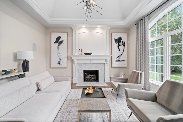 living area with a chandelier, a raised ceiling, crown molding, and a high end fireplace