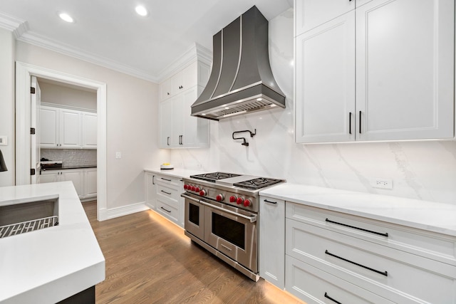 kitchen with white cabinets, ornamental molding, wall chimney range hood, double oven range, and dark wood finished floors