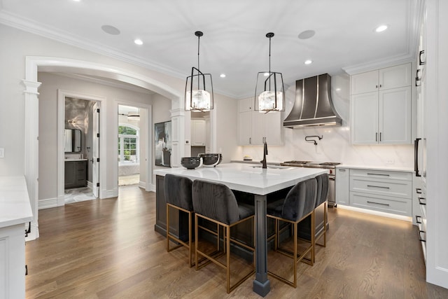 kitchen featuring arched walkways, white cabinets, wall chimney exhaust hood, ornamental molding, and dark wood-type flooring