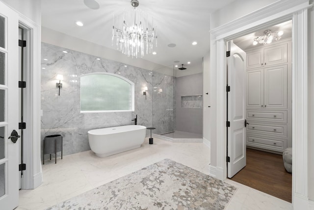 full bathroom with a marble finish shower, a soaking tub, marble finish floor, an inviting chandelier, and tile walls