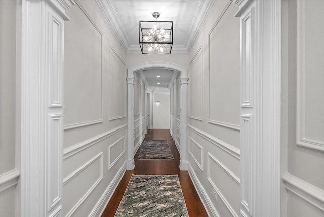 hallway with arched walkways, dark wood-style floors, ornamental molding, a decorative wall, and a notable chandelier