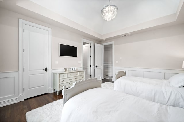 bedroom featuring a wainscoted wall, a chandelier, a raised ceiling, and dark wood-style flooring