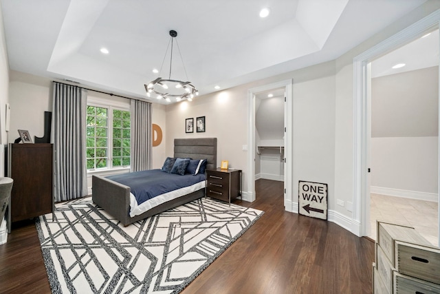 bedroom featuring a spacious closet, a tray ceiling, wood finished floors, and baseboards