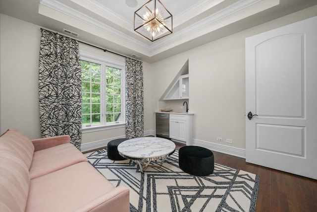 living area with dark wood-style floors, a raised ceiling, an inviting chandelier, ornamental molding, and wet bar