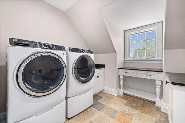 washroom with cabinet space, stone finish flooring, baseboards, and washing machine and clothes dryer